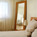 Cozy bedroom interior with a large wood framed mirror leaning against the wall, creating a warm and inviting atmosphere.