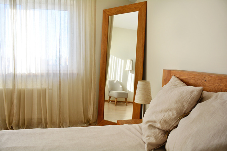 Cozy bedroom interior with a large wood framed mirror leaning against the wall, creating a warm and inviting atmosphere.