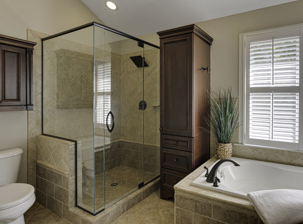 An elegant bathroom featuring a frameless glass shower enclosure; the elegant glass & shower mirrors reflect natural light from the shuttered windows onto earth-toned stone tiles.