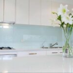 Modern kitchen interior with glossy glass backsplash and reflective surfaces, illustrating what type of glass is used for mirrors in residential design.