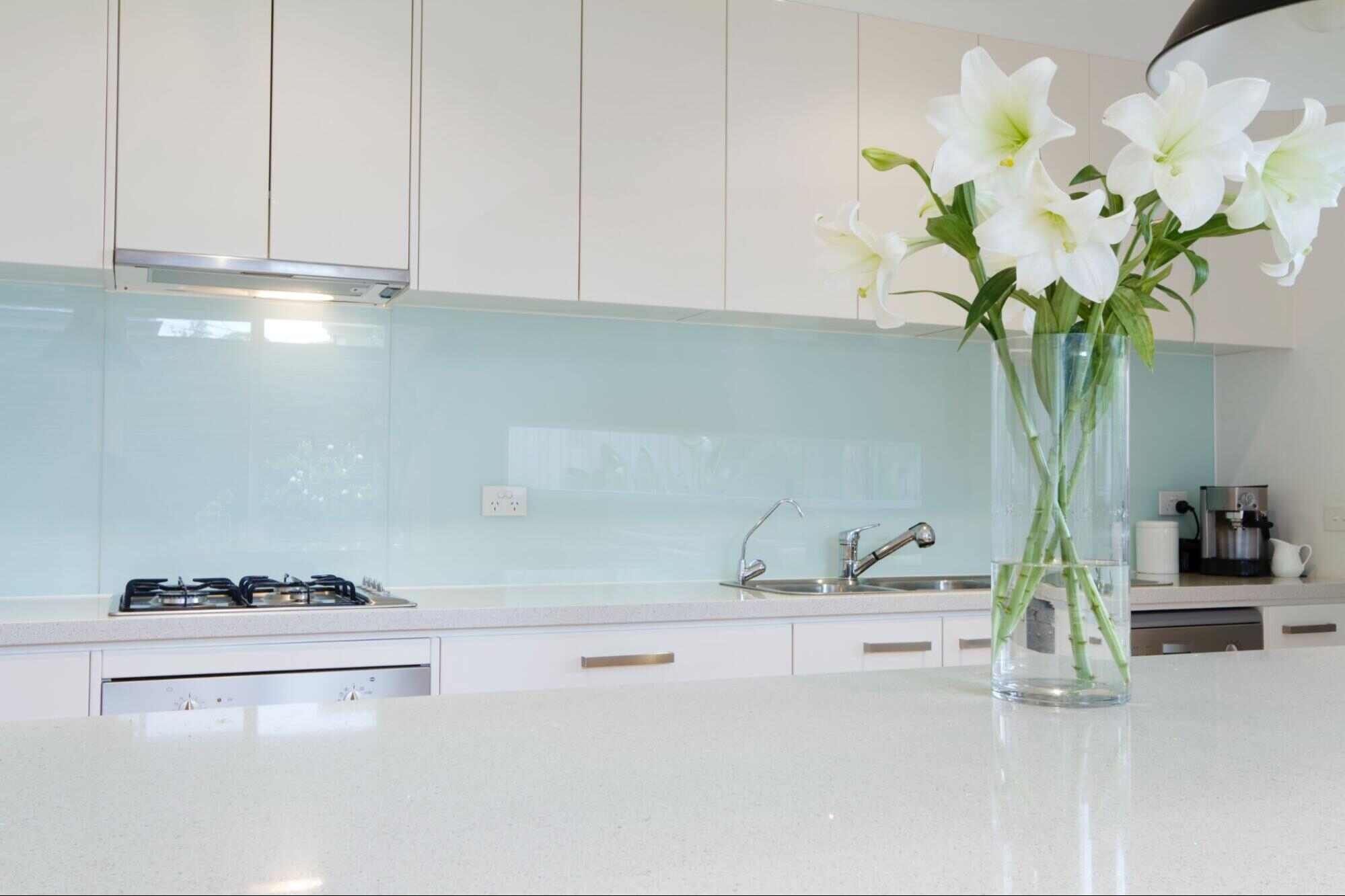 Modern kitchen interior with glossy glass backsplash and reflective surfaces, illustrating what type of glass is used for mirrors in residential design.
