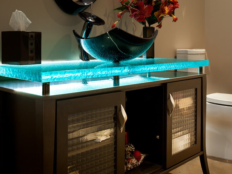 Custom kiln-formed glass countertop with integrated LED lighting and vessel sink for homeowners researching how much are kiln-formed glass countertops.