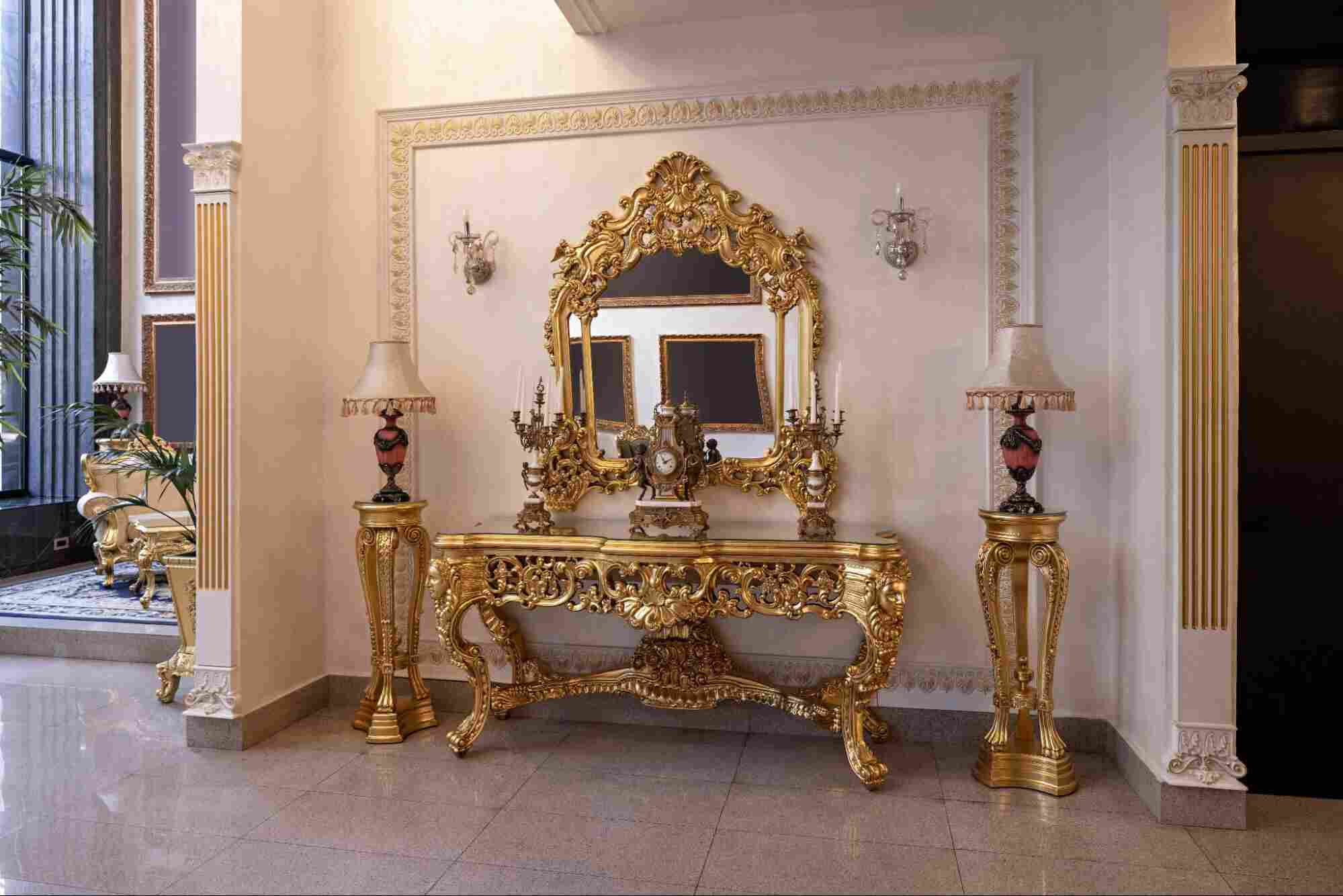 Ornate gold-framed antique mirror above an intricately carved console table in a luxurious foyer, showcasing the timeless elegance and craftsmanship of different types of antique mirrors in classic interior design.